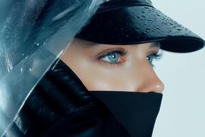 A model showcases captivating blue eyes while dressed in a black cap and mask. Raindrops accentuate her look, creating a moody and atmospheric vibe photo