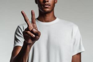 Man makes peace sign with hand in a neutral background while wearing a plain t-shirt photo