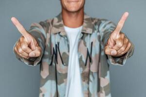 Man in a camouflage jacket making a hand gesture against a plain background in a casual indoor setting photo