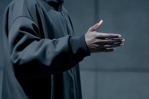 Person gesturing with hand in dark clothing against a minimalist backdrop during an interaction photo