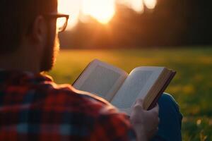 Person enjoys reading a book while sitting on grass during sunset in a peaceful outdoor setting photo