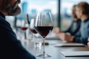 Group of individuals enjoying wine tasting with elegant glass of red wine in focus near window photo