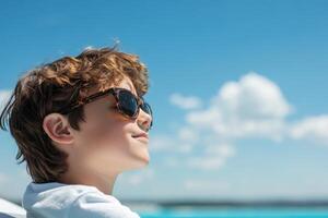 Young boy enjoys sunny day outdoors with sunglasses on by the water, capturing a moment of relaxation and joy photo