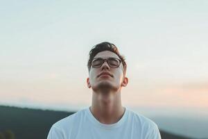 Young man enjoys serene moment outdoors at sunset while wearing glasses, embracing tranquility in nature photo