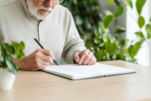 Elderly man writing in a notebook surrounded by indoor plants in a calm and serene environment photo