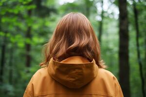 Person in a brown jacket stands in a lush green forest surrounded by tall trees and vibrant foliage on a calm day photo