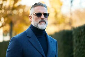 Stylish man outdoors during autumn, wearing sunglasses and a chic blue coat in a serene park setting photo
