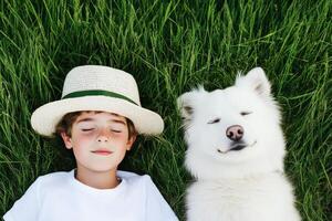 Boy enjoys a sunny afternoon while lying in grass next to smiling dog on a warm day photo