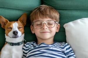 Boy relaxes on a green couch next to a dog taking a nap in a cozy setting photo