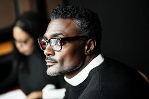 Thoughtful man in glasses engaged in conversation at cafe during evening hours photo