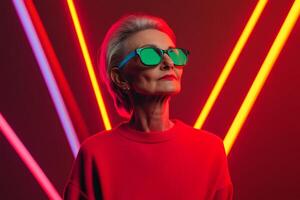 Stylish senior woman poses confidently in vibrant neon light setting with striking green sunglasses and red attire photo
