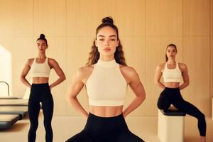 Three women in matching athletic outfits engage in yoga poses within a modern studio. Natural light fills the space, enhancing their focus and strength photo
