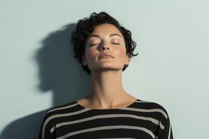 Calm woman with short curly hair relaxing against a light blue wall during daytime photo