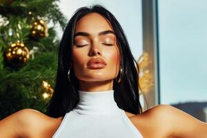 Model poses elegantly indoors with closed eyes in front of a decorated Christmas tree during a holiday photo shoot