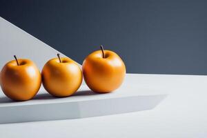 Three golden apples displayed on a white geometric platform against a contrasting dark background in a minimalist setting photo