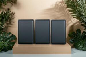 Stylish display of three sleek black objects set against a warm beige background with tropical green plants photo