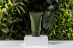Product display of a green tube on a white pedestal set against a lush green background showcasing natural beauty and eco-friendly themes photo