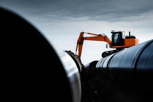 Excavator working on pipeline construction project under cloudy sky in industrial area photo