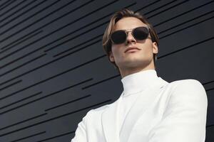 Stylish individual posing confidently in a white outfit under bright sunlight against a modern building backdrop photo