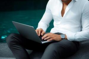 Professional man working on a laptop by a tranquil poolside during a sunny day photo
