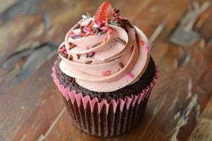 A chocolate cupcake with pink frosting and sprinkles photo