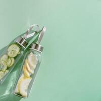 Top view two glass bottles, water drink detox with lemon and cucumber at sunlight on green background, copy space. Infused water with slices fruit or vegetable. Aesthetic photo with fresh drink