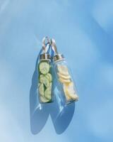 Top view two glass bottles, water drink detox with lemon and cucumber at sunlight on blue background, copy space. Infused water with slices fruit or vegetable. Aesthetic photo fresh drink