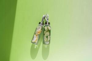 Lemon and cucumber water drink detox in glass bottle at sunlight on green background. Wellness, diet, eating healthy concept. Stylish reusable water bottle, eco friendly lifestyle minimal photo