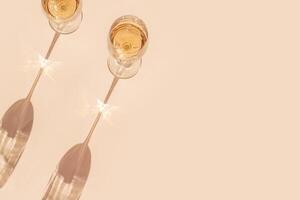 Sunlight still life with two glasses of white wine, beige background with shadow and glare, caustic light effect at sun. Minimal aesthetic trend photo with summer alcohol drink, dark light, above