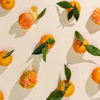 Tangerines as minimal creative pattern, juice fresh orange yellow fruits with green leaves on beige background. Citrus mandarines as still life food, trend flat lay, summer aesthetic photo