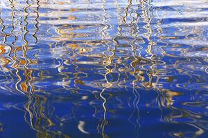 Dry reeds and their water reflections, nature landscape yellow blue vivid colors. Growing grass or plants in lake or wetlands, abstract natural background of reflects curved lines on water photo