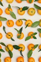 Fresh juicy orange yellow tangerines as minimal flat lay pattern, Citrus fruits with green leaves on beige table background. Still life creative trend pattern of mandarin oranges overhead view photo