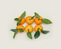 Set of Tangerines, minimal creative pattern, Ripe fresh orange yellow fruits with green leaves on beige background. Citrus mandarines as still life food, trend flat lay style, summer aesthetic photo