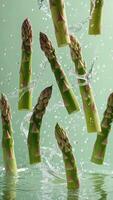 Fresh asparagus stalks are suspended mid-air, surrounded by splashing water against a light green backdrop, capturing a moment of freshness. photo