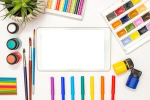 White digital tablet with a blank screen on table and drawing supplies photo