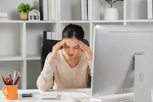 Woman experiencing stress and headaches while working at a computer in an office. photo