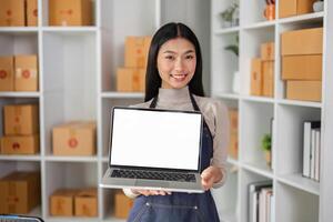 Smiling young female entrepreneur presenting a laptop in a modern workspace, promoting her business. photo
