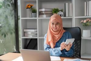 Muslim woman using calculator and laptop while analyzing financial data in a modern workspace. photo