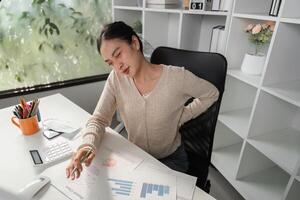 Woman with back pain at desk while analyzing financial charts and graphs. photo