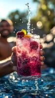 Hand holding refreshing raspberry cocktail with splashing water by the pool photo