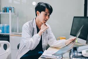 A man in a lab coat is sitting at a desk with a computer photo
