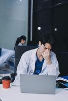 A man in a lab coat sitting at a desk with a laptop photo