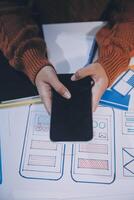 A person using a smartphone on a desk with a lot of design and coding photo