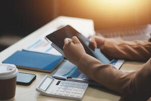 A person is using a tablet on a desk with a coffee cup and calculator photo