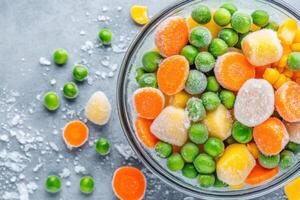 Vibrant frozen vegetables including peas, carrots, and corn arranged in a frost-covered glass bowl viewed from above photo