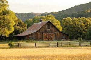 Rustic barn stands in golden field at sunset with lush green hills in background photo