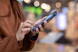 Close-up of hands interacting with a smartphone in a busy shopping mall. Background features colorful bokeh lights creating a lively, modern atmosphere, emphasizing connectivity, technology photo