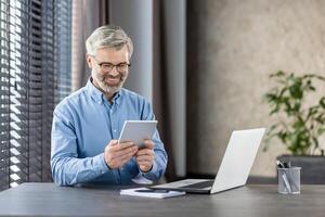 Senior professional using tablet while smiling in modern office. Concept of technology, work, senior business professional utilizing digital devices photo