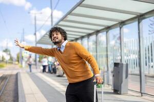 Passenger with suitcase trying to stop bus or taxi. Man standing waving hand, tourist traveling. photo