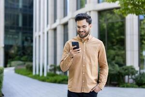 Smiling man using smartphone outdoors in urban environment. Man in casual attire enjoying technology and communication while walking in city setting. Concept of modern lifestyle, connectivity photo